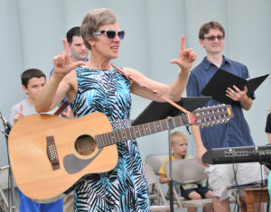 Lindsay Steele  Diane Mahoney, director of music for Ss. John & Paul Parish in Burlington, directs the crowd during Mass at Crapo Park in Burlington Aug. 8. In its second year, Faith Fest helped inspire Catholics and non-Catholics alike.