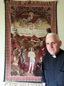 Contributed Father William Kneemiller stands in front of a tapestry from Jordan that he brought back to the United States after one of his tours as a military chaplain overseas.