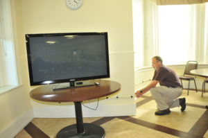 Lindsay Steele Rob Butterworth, technology director for the Diocese of Dav­enport, sets up a television in the dining room of the St. Vincent Center in Davenport so retired priests will be able to view events from the papal visit. He is securing the wires so people won’t trip.