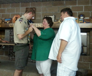 T. Waldmann-Williams Patty Schwanebeck pins the Eagle Scout emblem onto her son, Cris Patrick, Aug. 16 at Camp Collins in Knoxville, as Cris Patrick’s father, Cris, looks on.