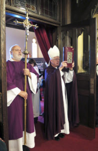 Anne Marie Amacher Bishop Martin Amos holds the Book of the Gospels after opening the Doors of Mercy at Sacred Heart Cathedral in Davenport Dec. 13. Deacon David Montgomery holds the cross to begin the procession. 