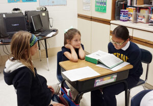 Nita Carlson Sixth-graders Elle Rheinschmidt and Elisabeth Blanco teach a Bible story to second-grader Addison Cardin, center, at Notre Dame Catholics Schools in Burlington Oct. 5. It is a tradition for sixth-graders at Notre Dame to mentor second-graders and pray with them throughout the year.