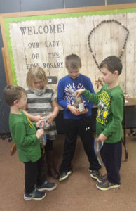 Bev Brauer Parker, Delanee, Declan and Eli, religious education students at Our Lady of the Holy Rosary Parish-Lost Nation, put change in jars Feb. 4. Parish youths initiated a parish Lenten almsgiving project of raising money for Food for the Poor.  