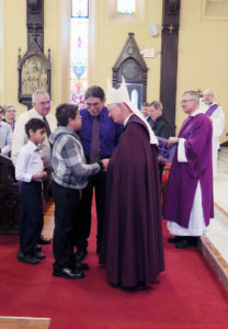 Anne Marie Amacher Lukas Hill and his sponsor Tom Simmons are greeted by Bishop Martin Amos during the Rite of Election and Call to Continuing Conversion Feb. 14 at Sacred Heart Cathedral in Davenport. Waiting their turn are Zarius Hill and his sponsor Sam Guzzo. Both are entering the church through Our Lady of Victory Parish in Davenport.