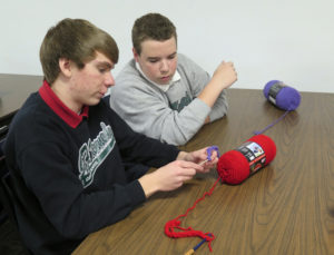 Anne Marie Amacher Zach Wemhoff, left, helps fellow eighth-grader Brett Rappel with a crochet technique. Eighth-graders at John F. Kennedy Catholic School and Our Lady of Victory religious education program in Davenport crocheted scarves to help the homeless and others stay warm during cold weather. 