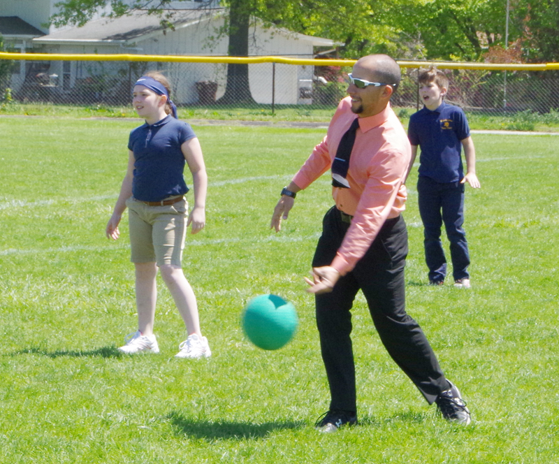 Ron Teater Chris Schwarz, assistant principal of Notre Dame Catholic Schools in Burlington rolls a pitch during a recess kickball game earlier this month. Fielding are fourth-graders Ella Corzatt and Spencer Brent. 