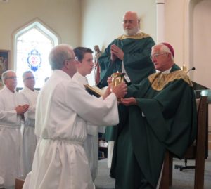 Anne Marie Amacher Deacon candidate Joe Rohret of St. Peter Parish, Cosgrove, receives a flagon of wine from Bishop Martin Amos during the Rite of Institution of Acolytes. The Mass was held June 11 at St. Paul the Apostle Church in Davenport. Assisting the bishop is Deacon David Montgomery.