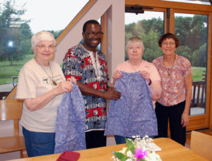 contributed Sister Teresa Kunkel, left, and Sister Virginia Krakow hold dresses designed and sewn for Joshua Ngao, center, to carry with him on his upcoming trip to Kenya. Ngao, president and CEO of Fishers for Men Ministries in Davenport (FOM), spoke to the Sisters of St. Francis at The Canticle July 20 about the organization. Also pictured is Sister Jeanne d’Arc Untz.