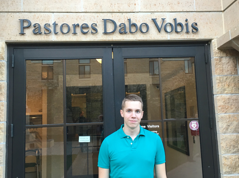 Contributed Seminarian Dale Mallory stands in front of the St. Paul Seminary entrance in St. Paul, Minn. The sign above him translates “I Will Give You Shepherds.” 